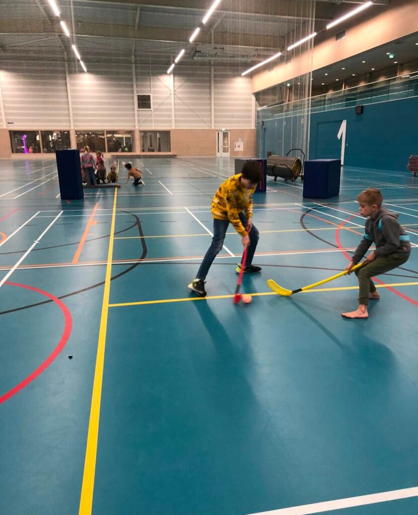 kinderen spelen hockey in de gymzaal bij Sport-BSO Flekss